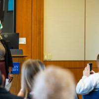 woman holding microphone presenting to full room "Teach-In" banner next to her